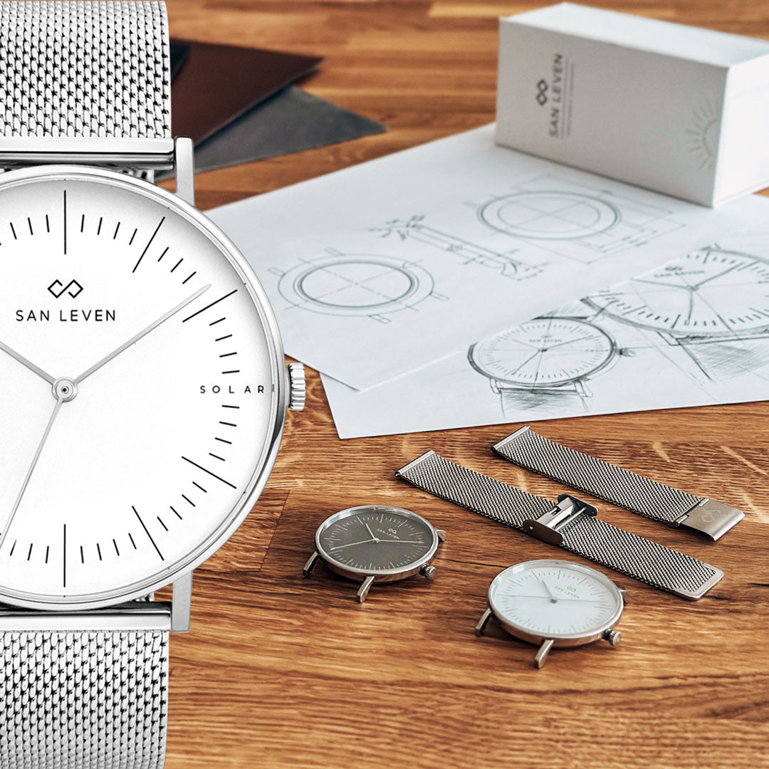 SPARK Solaruhr mit Mesh-Armband neben handgezeichneten Konstruktionsskizzen und Verpackung